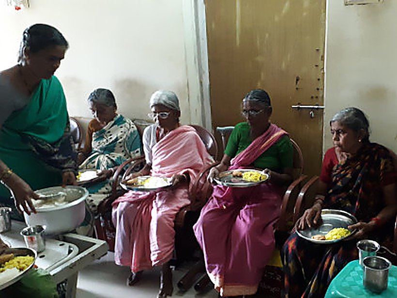 A volunteer serves a warm lunch to elders seated together at the centre.