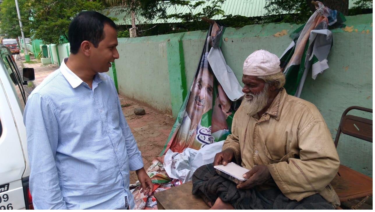 A Karuna volunteer speaks with an elderly man on the street, sharing food and conversation.
