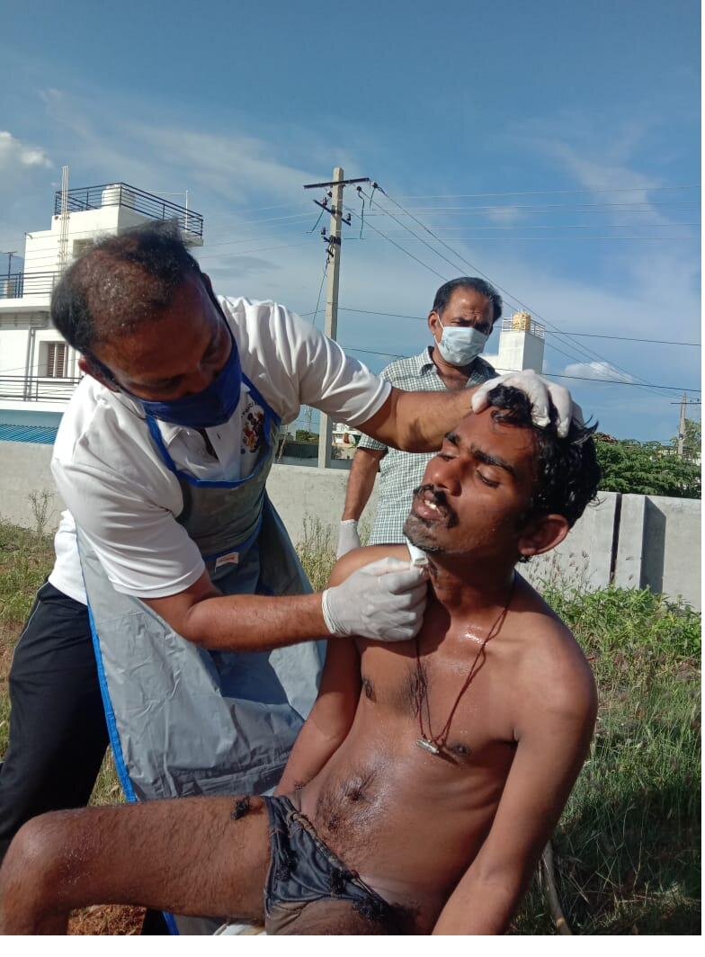 A Karuna volunteer carefully bathes and grooms a young man in the open air, restoring his dignity.