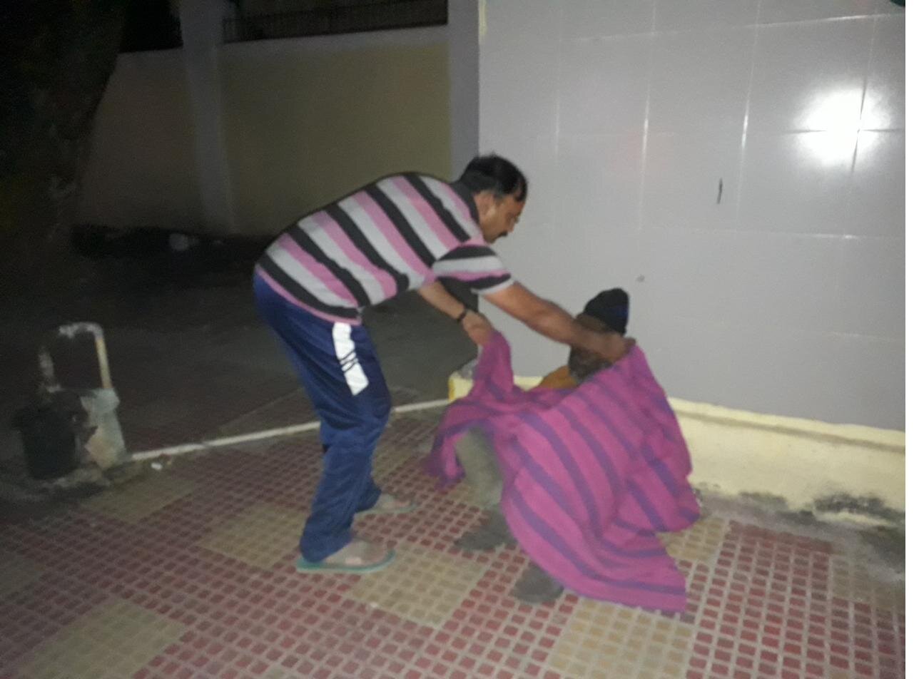 At night, a Karuna volunteer wraps a warm blanket around a homeless man on the street.
